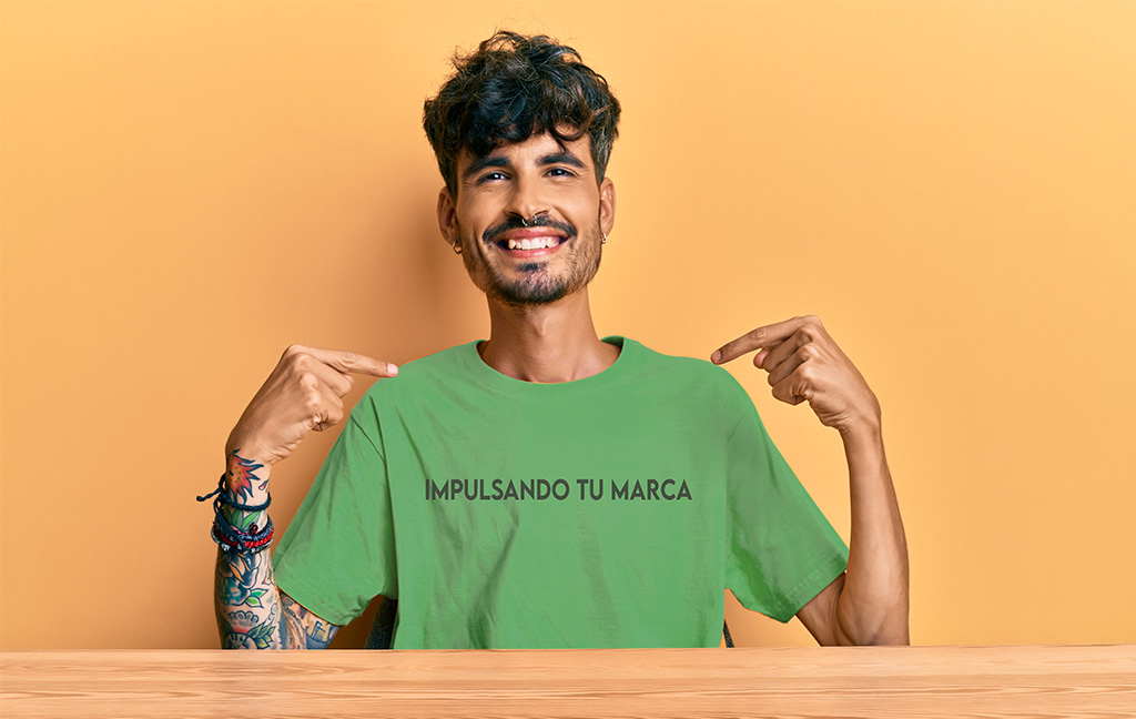 Hombre sonriente apuntando a su playera con la frase impulsa tu marca
